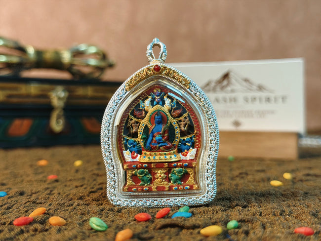 Medicine Buddha Tsa Tsa Gau pendant, front view on textured brown cloth.