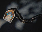 Five Jambhalas pendant with a dark beaded necklace on fabric