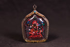 Palden Lhamo side of a double-sided Tsa Tsa pendant on a dark background