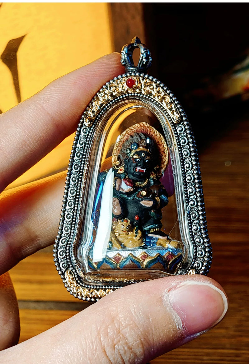 Black Jambhala pendant held between fingers for scale