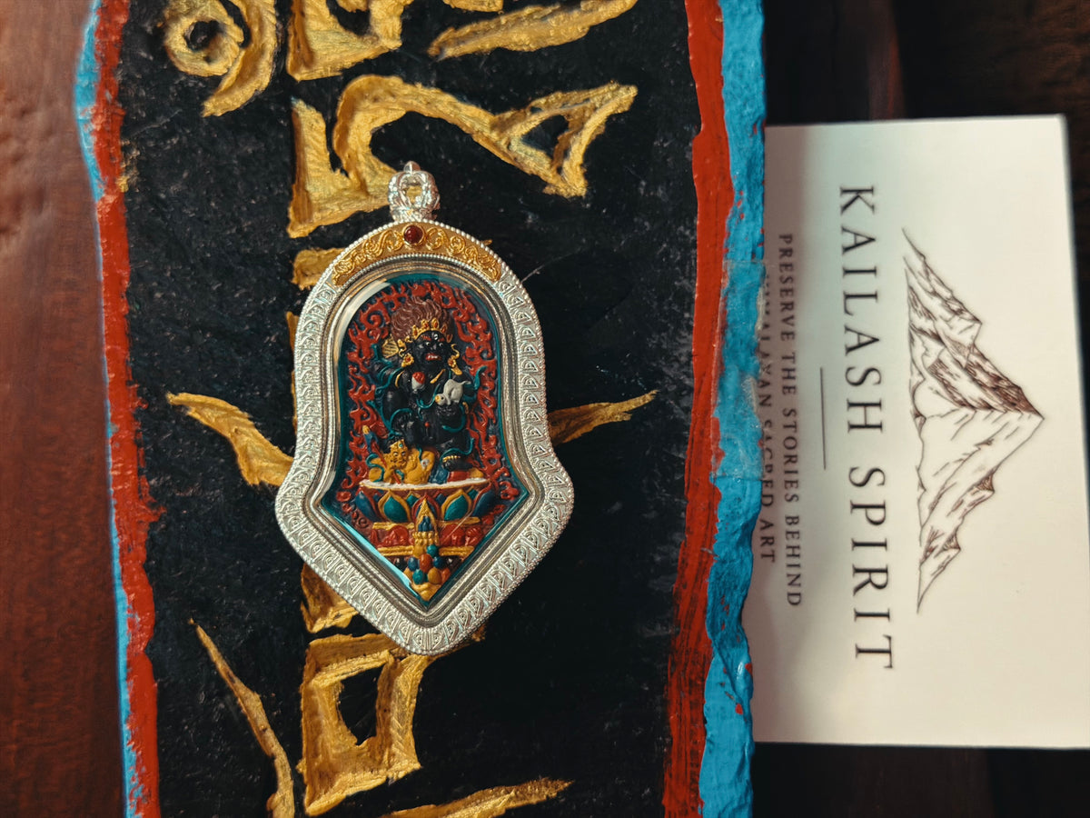 Black Jambhala tsa tsa pendant displayed on Tibetan script cloth with a Kailash Spirit card