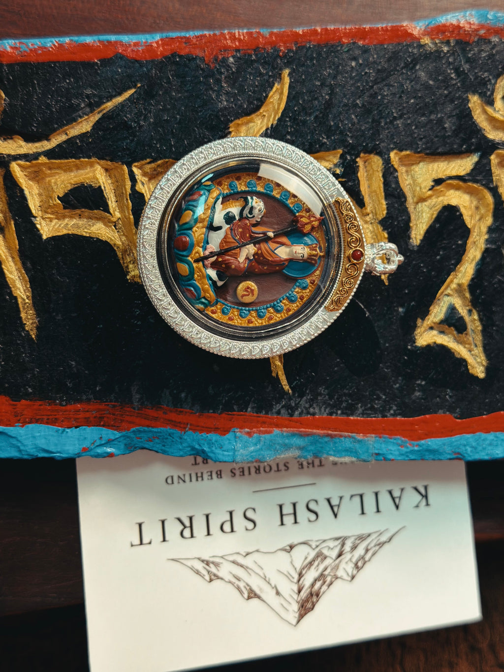 Round Ksitigarbha tsa tsa pendant displayed on Tibetan script cloth with a Kailash Spirit card